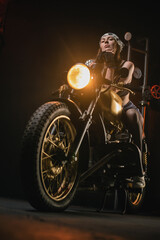 Fototapeta na wymiar Girl motorbiker in the bandana and black top posing on the old retro motorbike.