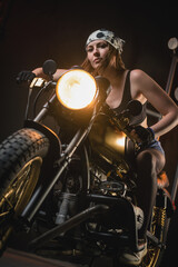 Plakat Girl motorbiker in the bandana and black top posing on the old retro motorbike.