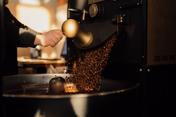 Crop anonymous male worker pressing lever and roasted coffee beans pouring from release chute in...