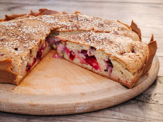 Rustic homemade cherry and cherry plum pie sprinkled with sesame seeds on a round cutting board on an old wooden table close-up. Country style