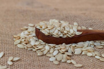 Fototapeta na wymiar Char Magaz or Dried Melon Seeds in a Wooden Spoon Isolated on Burlap Fabric