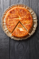Kouign amann is a round multi-layered cake containing with laminated dough soaked in butter and sugar closeup on the plate on the table. Vertical top view from above