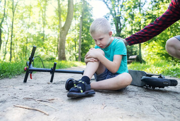 Kid fall when riding an electric scooter. Riding an e-scooter without protective gear. Increased risk of injury when using battery powered vehicles. Mom gives first aid for a knee injury