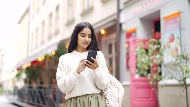 Attractive young hispanic indian young woman tourist walking on city street lady using smartphone mobile cell phone Outdoor browsing internet, searching Technology and lifestyle travel trip journey