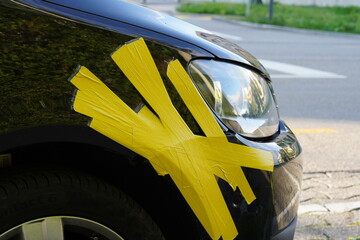 Damaged front fender of the black car in close view. Front mudguard is fixed with yellow adhesive...