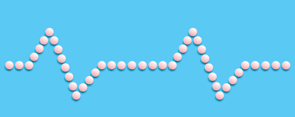 A group of pink round pills forms a pulse line on a blue background. The theme of healthcare, treatment and prevention of diseases. World Heart Day