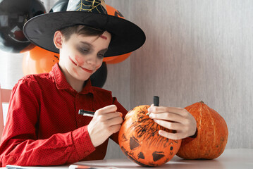 Teen boy in costume drawing coronavirus image on the pumpkin for the Halloween celebration....