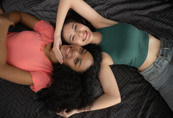 Top view of two young women lying on bed and smiling at each other