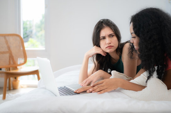Both of  young women use laptops to browse information and contact friends online in bedroom of the house. LGBT concept.