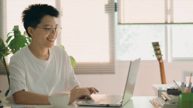 Smiling Asian man in glasses hand typing online report working on a laptop device. work from an office home