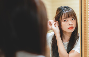 Fototapeta premium Young asian woman is dressing up and wearing earrings in front of a mirror in bathroom