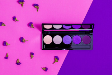 Makeup eyeshadow palette with limonium flowers on the purple and pink background. Makeup eyeshadow palette set.