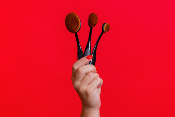 Makeup brushes in woman hand on the red background. Makeup brushes set.