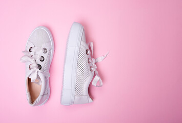 Modern white casual sneakers from perforated leather isolated on a soft pink background with copy space. Fashion blog or magazine concept. Top view