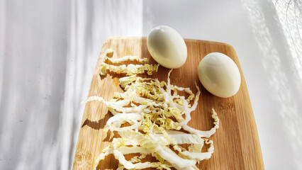 Chopped Peking cabbage and peeled eggs on cutting board as a background. Cooking a healthy eco-friendly salad from natural products. Copy space and place for text