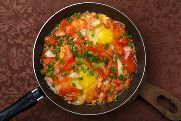 hot shakshuka in a frying pan sprinkled with green onions on a wooden board.