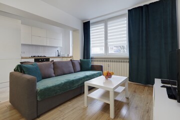 Nowoczesny apartament z zielona sofą, telewizorem i otwartą kuchnią