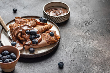 Chocolate crepes with blueberry and chocolate paste on brown textured background rustic style with text space