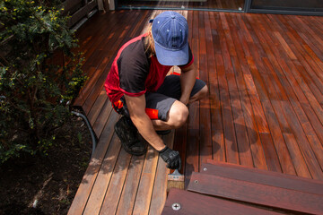 Ipe hardwood deck annual refreshing, man with paintbrush applying natural nourishing oil on cleaned...
