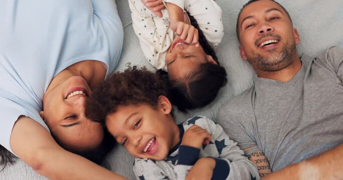 Above, playful and a family on the bed for tickling, love and comedy in the morning. Happy, laughing and parents playing with funny children in a home bedroom for bonding, care and crazy together
