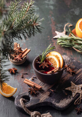 Mulled wine in brown ceramic mug with orange slices and spices. Christmas hot drink on wooden table with xmas tree branches, festive card