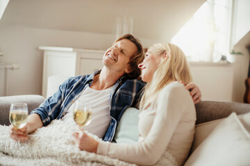 Mature couple enjoying a glass of wine under a blanket on the couch in the living room