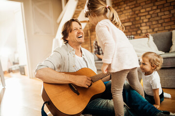 Young family playing together in the living room while the father is playing the guitar