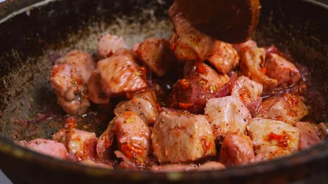 Chicken pieces with red onion and spices in sauce in a frying pan are mixed with a wooden spatula