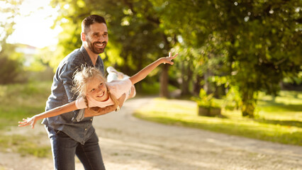 Happy european father lifting daughter in air playing and having fun together in park, panorama,...