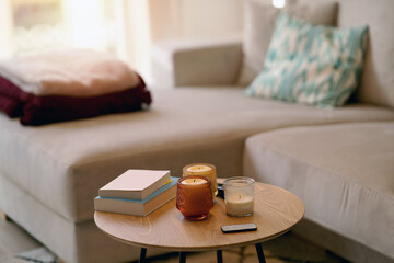 Books candle lights remote controller on round table near sofa in daylight