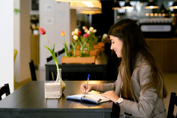 Focused young woman sitting at table and making notes in cafe
