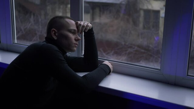 Guy looking out of window. Frustrated young man thinking or personal problems solution, regretting mistakes, suffering from depression or divorce break up relations, feeling lonely at home.