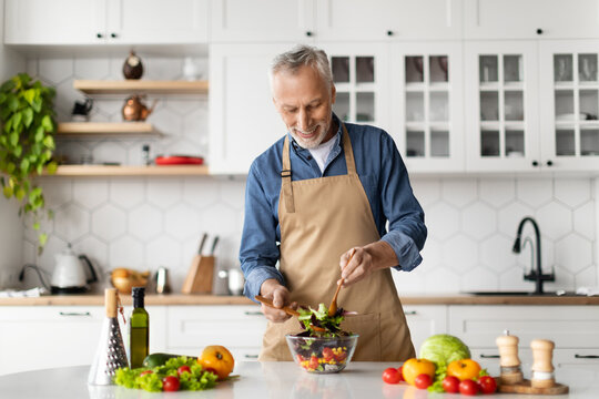 Healthy Nutrition Concept. Happy Senior Man Cooking Fresh Vegetable Salad In Kitchen