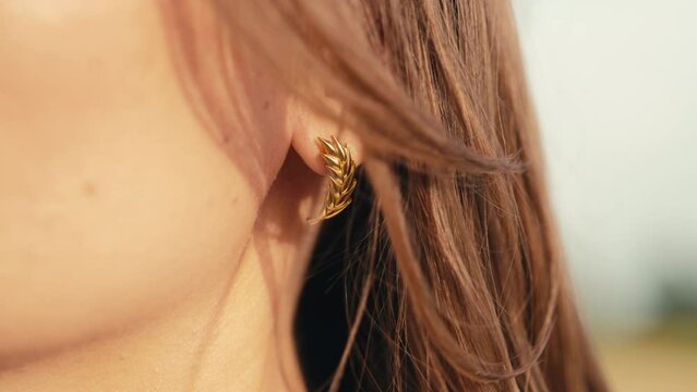 Young woman with gold wheatear earrings posing outdoors. Jewelry details