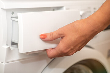 A woman opens the tray for pouring laundry detergent into the washing machine. The concept of...