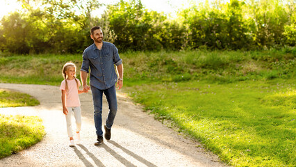 Dad walking with his daughter holding hands and looking aside at free space, family enjoying stroll...