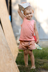 A little blond boy paints the wall with a roller.A kid in a T-shirt, shorts and a paper hat in the...