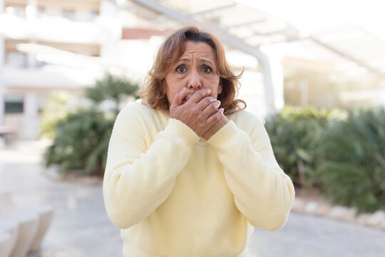 middle age woman covering mouth with hands with a shocked, surprised expression, keeping a secret or saying oops
