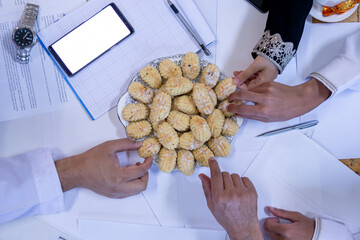 Arabic working colleagues hands  eating eid kahk together on working desk