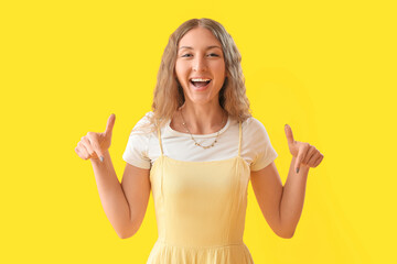 Beautiful young woman pointing at something on yellow background