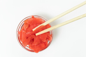 Transparent bowl with pickled ginger and wooden chopsticks for eating. View from above the components for creating sushi on white surface.