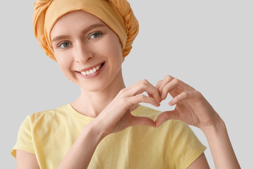 Teenage girl after chemotherapy making heart with her hands on light background, closeup