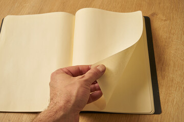 A white male hand turning the blank pages of a diary, notebook.