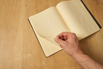 A white male hand turning the blank pages of a diary, notebook.