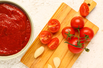 Bowl with tasty tomato paste and fresh vegetables on light background, closeup