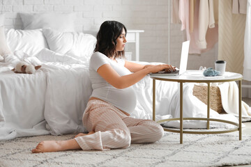 Young pregnant woman working with laptop in bedroom