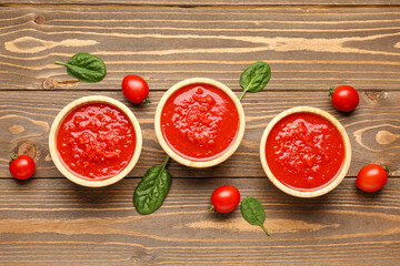 Bowls with tasty tomato sauce and fresh vegetables on wooden background