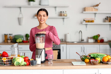 Sporty young woman making healthy smoothie with blender in kitchen