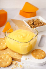 Bowls of tasty cheddar sauce with crackers, cheese chunks and walnuts on white grunge background