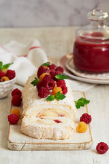 Meringue roll with butter cream and raspberry curd, decorated with berries on a light background.